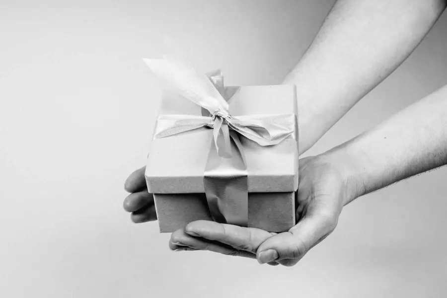 Mains tenant une boîte-cadeau en carton nouée d’un ruban